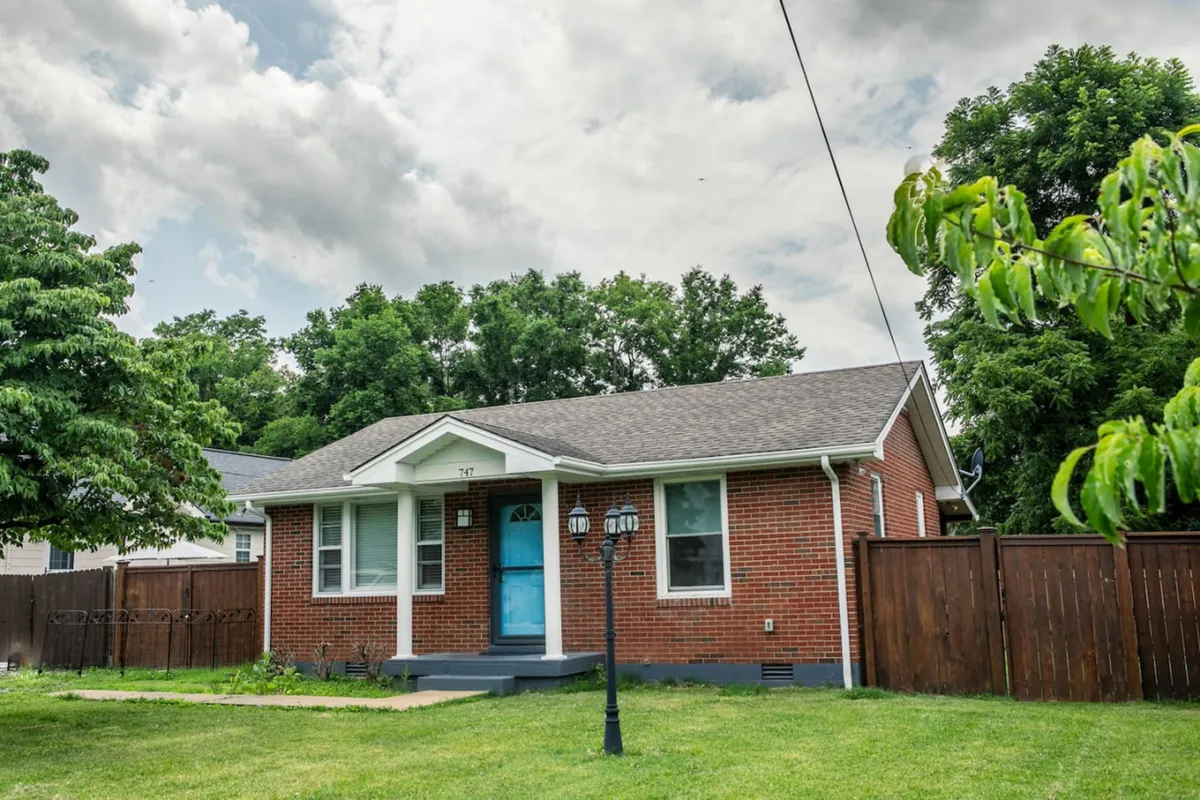 A welcoming brick facade with a blue door, accented by a lamp post and subtle landscaping. The front yard hints at a family-friendly atmosphere, perfect for gatherings and children's play. The inviting porch and open yard set the tone for a comfortable, home-like retreat.