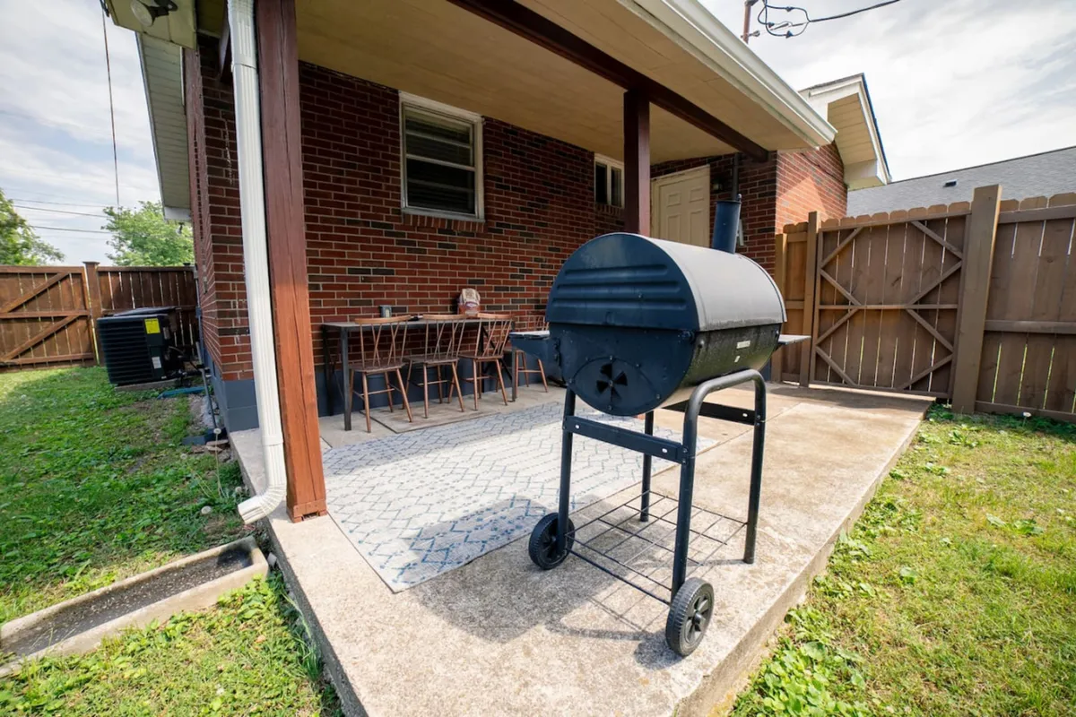 This image features a backyard setting focused on a grill, a dining table, and a wooden fence. The arrangement suggests a welcoming environment for barbecuing, outdoor dining, and relaxed socializing. The greenery surrounding the area adds privacy and a sense of tranquility.