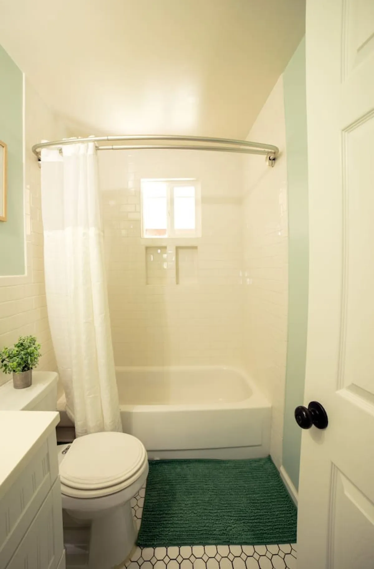A sparkling modern bathroom featuring a glass-enclosed shower area, toilet, a vibrant green rug, and a small plant for a fresh touch. The serene mood encourages relaxation and self-care routines, aligning with the idea of a personal sanctuary.