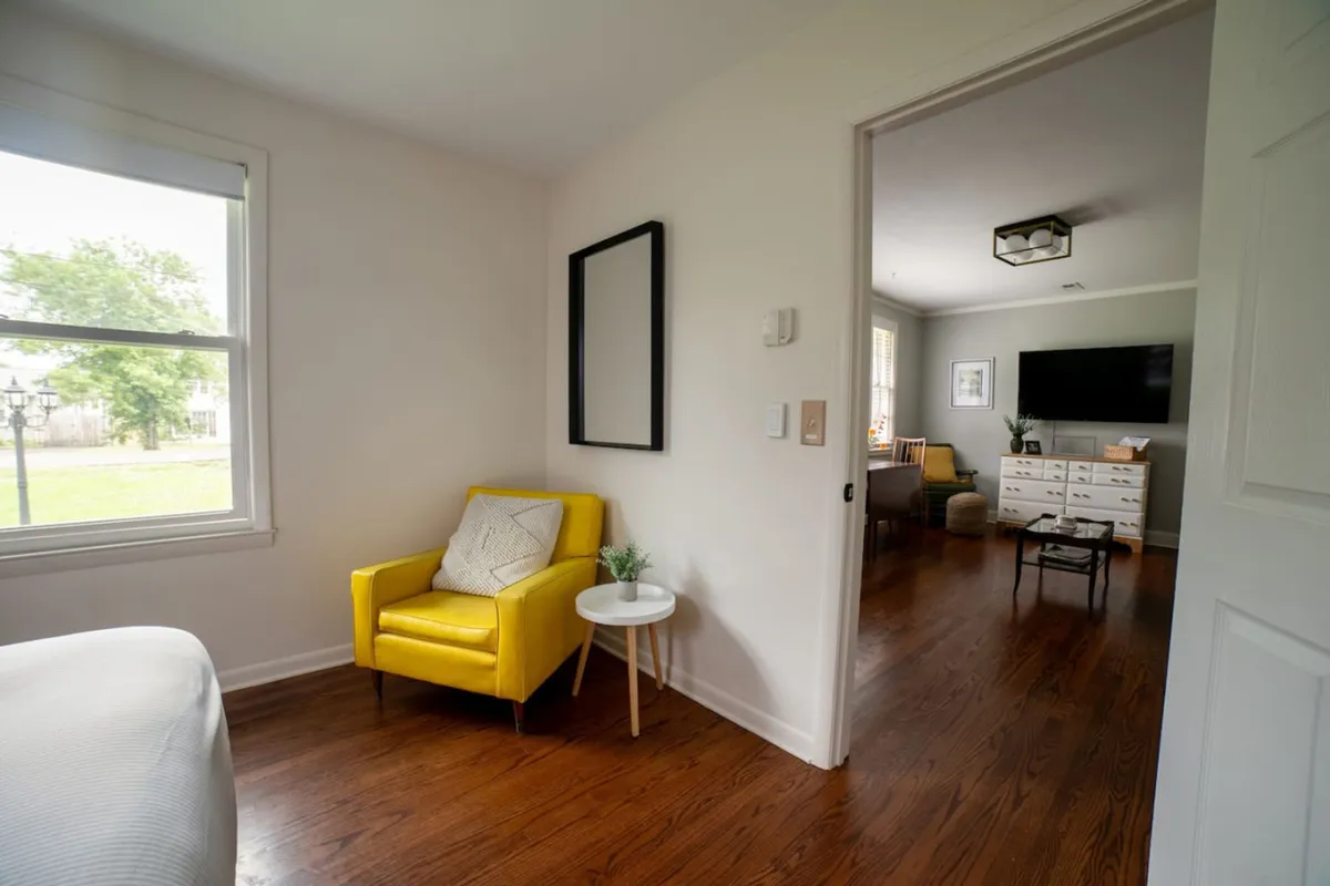A sunny corner with a cheerful yellow armchair, a side table perfect for coffee or reading, and a framed mirror reflecting light. The décor is warm and welcoming, creating a cozy nook within the central living space.