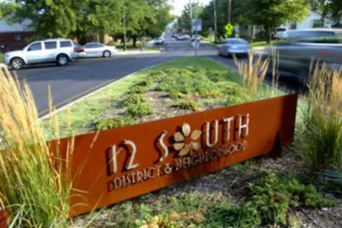 A welcoming street view of the 12 South district sign surrounded by landscape greenery and a bustling neighborhood vibe. The scene captures people enjoying the outdoors, exploring local shops, and soaking in the vibrant energy of one of Nashville’s most beloved neighborhoods.