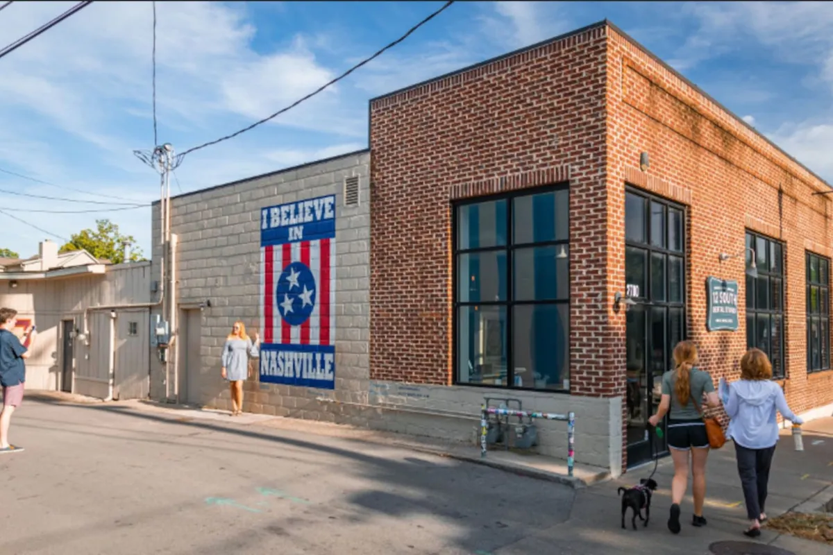 A bright exterior shot featuring a distinctive brick building facade with a mural of the Tennessee flag. The image includes people walking, evoking a sense of neighborhood activity and community, and emphasizes the walkability and welcoming atmosphere of the area.