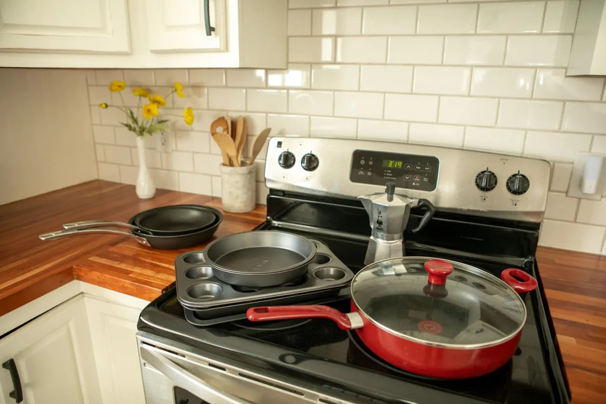 A cheerful kitchen scene with a red frying pan on a stainless steel stove, wooden countertops, a vase with yellow flowers, and a set of cookware. The area feels bright and homely, suggesting both functionality and a welcoming vibe for shared meals and celebrations.