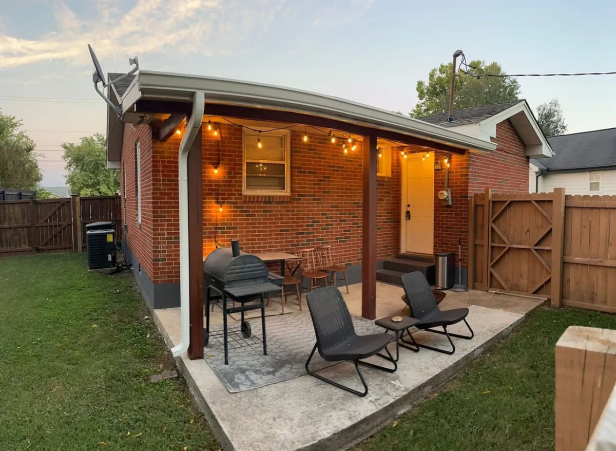 A cozy outdoor dining area with a grill, comfortable seating, string lights, and a brick wall backdrop. The space is designed for barbecues and relaxed evenings under the stars, embodying the spirit of family meals and socializing in the open air.