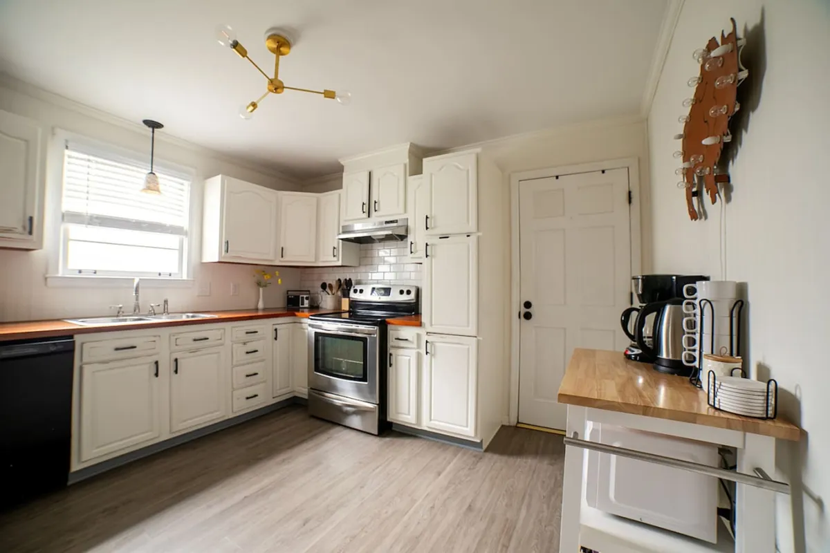A modern kitchen scene with stainless steel appliances, wooden countertops, white cabinetry, and stylish lighting. The kitchen’s open design encourages social cooking and group interaction.